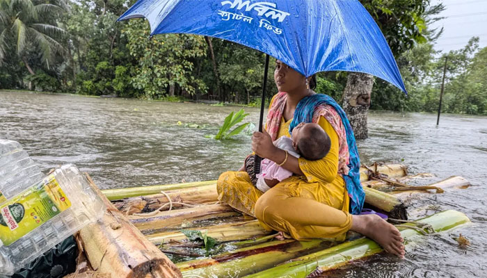 A woman and her child wade through flood waters in Feni, Bangladesh on August 22, 2024. — AFP