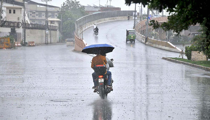 Young motorcyclists use an umbrella for protection from the rain during heavy rain in Multan on August 21, 2024. — APP