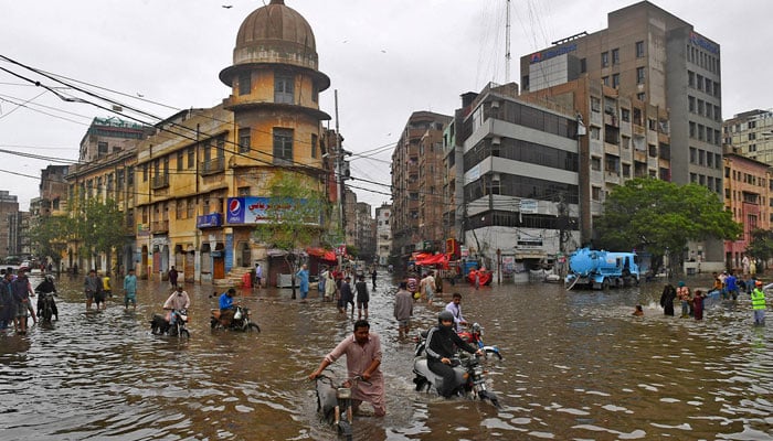 People wade across a flooded street after heavy monsoon rainfall in Karachi on July 25, 2022. — AFP/file