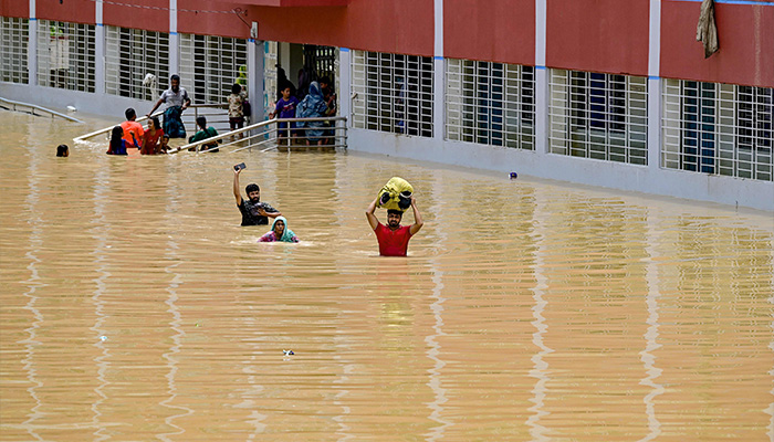 People wade through floodwaters outside a temporary shelter in Feni on August 24, 2024. — AFP