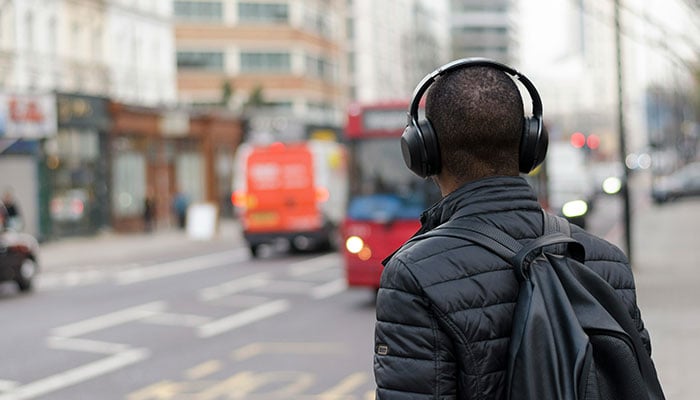 A represenatational image depicting a person wearing headphones while crossing a road in a city. — Unsplash/File