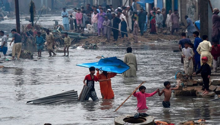 People wade through a flooded residential area after heavy monsoon rains in Karachi on August 27, 2020. — AFP