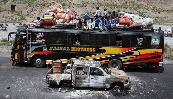 A bus with passengers sitting on the roof with belongings, drives past a damaged vehicle, a day after militants conducted deadly attacks, in Bolan district of Pakistans restive province of Balochistan, Pakistan August 27, 2024. — Reuters