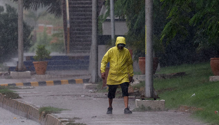 A man wears a rain jacket as he walks along a side walk during a rain in Karachi, Pakistan, August 2, 2024. — REUTERS