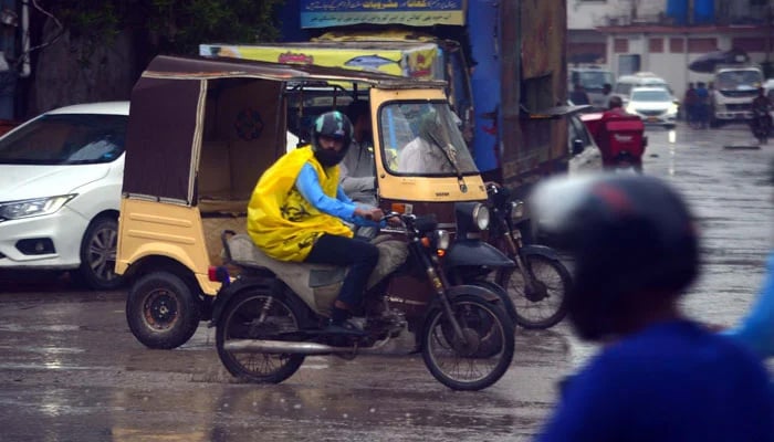 A motorist wearing raincoat drives across a road during the heavy downpour of monsoon season, near Shaheen Complex in Karachi on August 29, 2024. — PPI