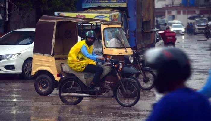 A motorist wearing raincoat drives across a road during the heavy downpour of monsoon season, near Shaheen Complex in Karachi on August 29, 2024. — PPI