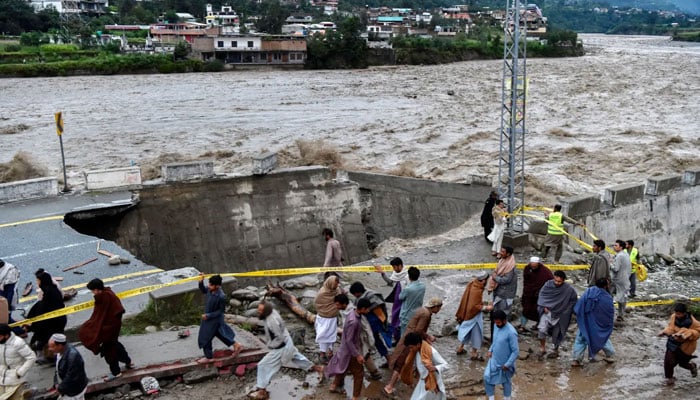 People move past a road washed out by floodwaters in Pakistan’s northern Swat Valley on August 27, 2022. — AFP