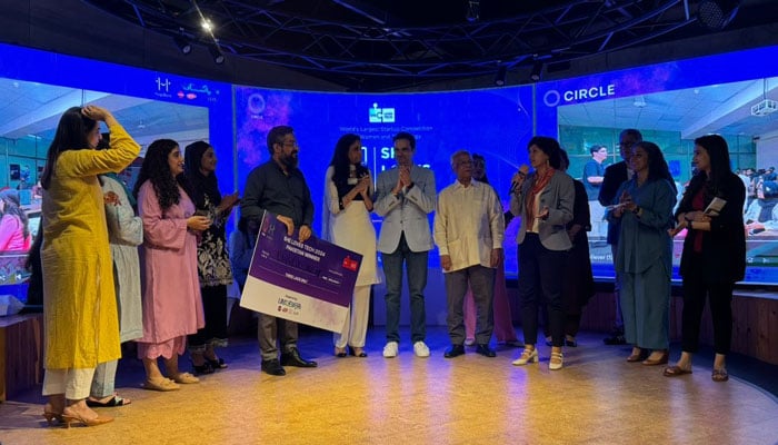 Islam un Nisas husband receives the winning prize as judges and guests stand on the stage. — Photo by author