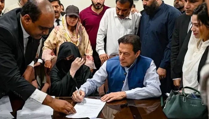 PTI founder Imran Khan (right) pictured along with his wife Bushra Bibi (centre) as he signs surety bonds for bail in various cases, at the registrars office in the Lahore High Court on July 17, 2023. — AFP