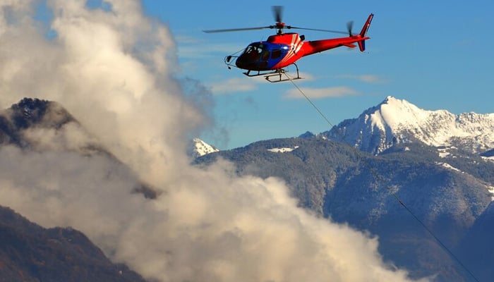 Representation image shows helicopter flying among the clouds above the snow-capped mountains. — Freepik