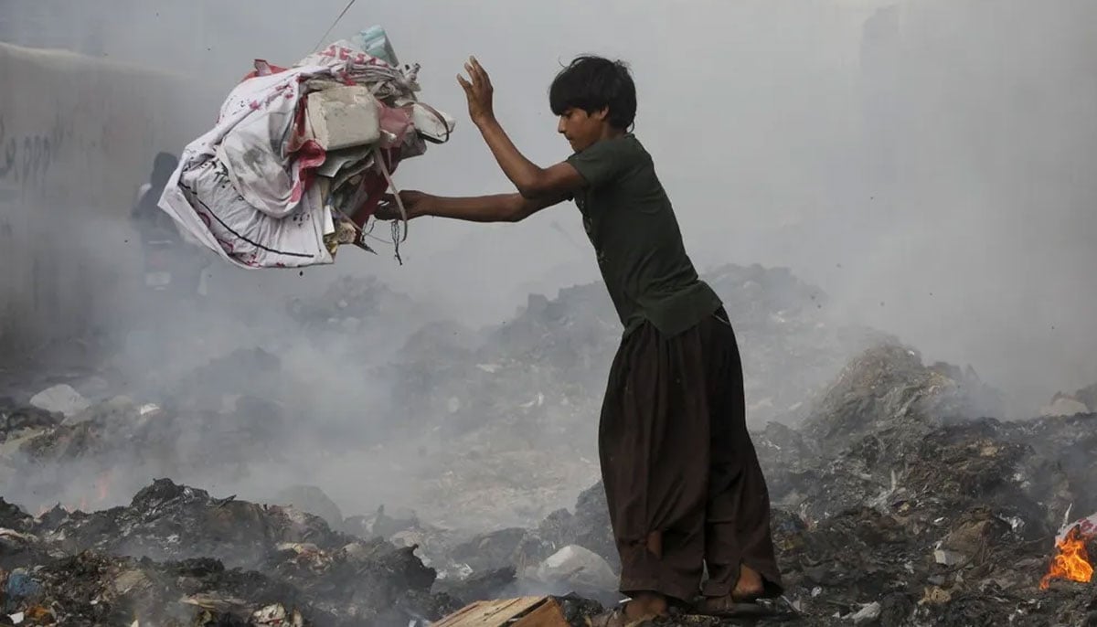 A boy throws a bundle of rubbish while searching for recyclables from the pile of smoldering garbage dump along a street in Karachi on July 31, 2015. — Reuters