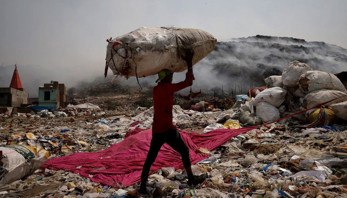 A waste collector carries recyclable materials as smoke billows from the burning rubbish at Bhalswa landfill site in Indias New Delhi. — Reuters/File