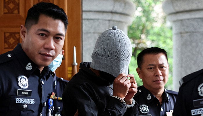 A man linked to Global Ikhwan Service and Business Holdings (GISB) covers his face as he is escorted by police officers after being charged in a court in Putrajaya, Malaysia September 18, 2024. — Reuters