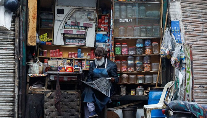 A man reads newspaper while selling betel leaves, known as pan, cigarettes and candies from a shop in Karachi on December 30, 2021. — Reuters