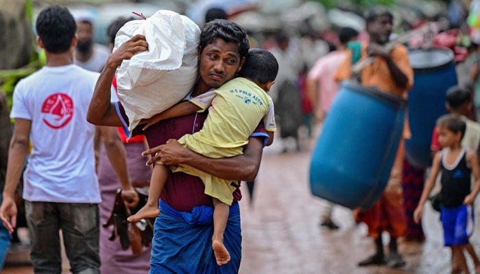 A Rohingya refugee man holds his child while carrying relief material at a camp in Ukhia on September 12, 2024. — AFP