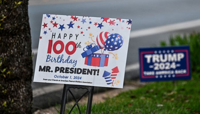 A placard celebrating former US President Jimmy Carter´s 100th birthday and a Trump campaign sign are displayed outside of a residence in Plains, Georgia, on September 30, 2024. — AFP