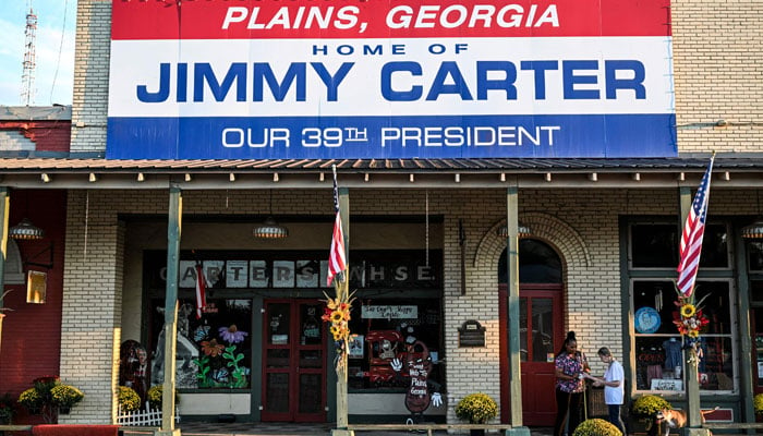 A local resident and friend of former US President Jimmy Carter Gloria English (right), along with her care taker Stacy Ludden, walk beneath a sign reading Home of Jimmy Carter in Plains, Georgia, on September 30, 2024. — AFP