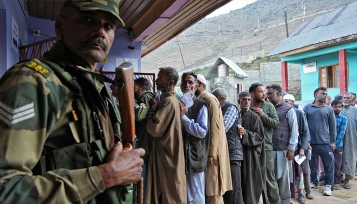 An Indian Border Security Force personnel stands guard as people wait a line to cast their vote outside a polling station during the third and final phase of the assembly election, in north Kashmirs Bandipora district October 1, 2024.