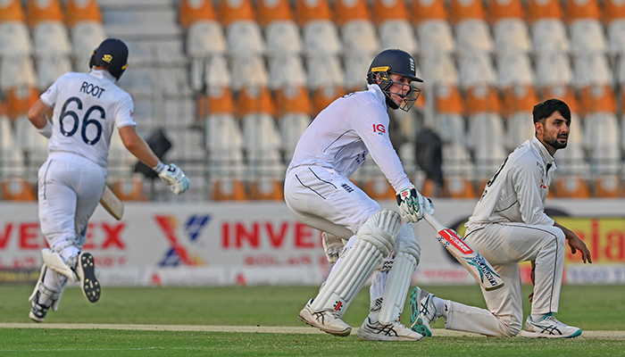 Englands Zak Crawley and Joe Root (L) run between the wickets as Pakistans Abrar Ahmed (R) watches during the second day of the first Test cricket match between Pakistan and England at the Multan Cricket Stadium in Multan on October 8, 2024. — AFP