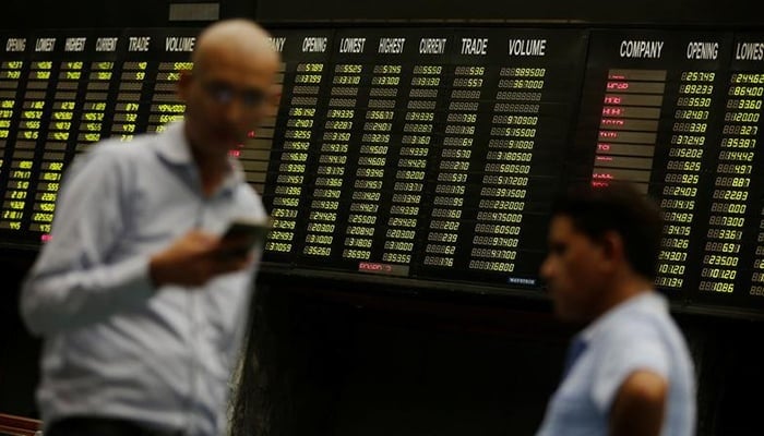 Men use their cell phones as they stand in front of electronic board displaying share market prices during a trading session in the halls of Pakistan Stock Exchange (PSX) in Karachi, on, June 12, 2017. — Reuters