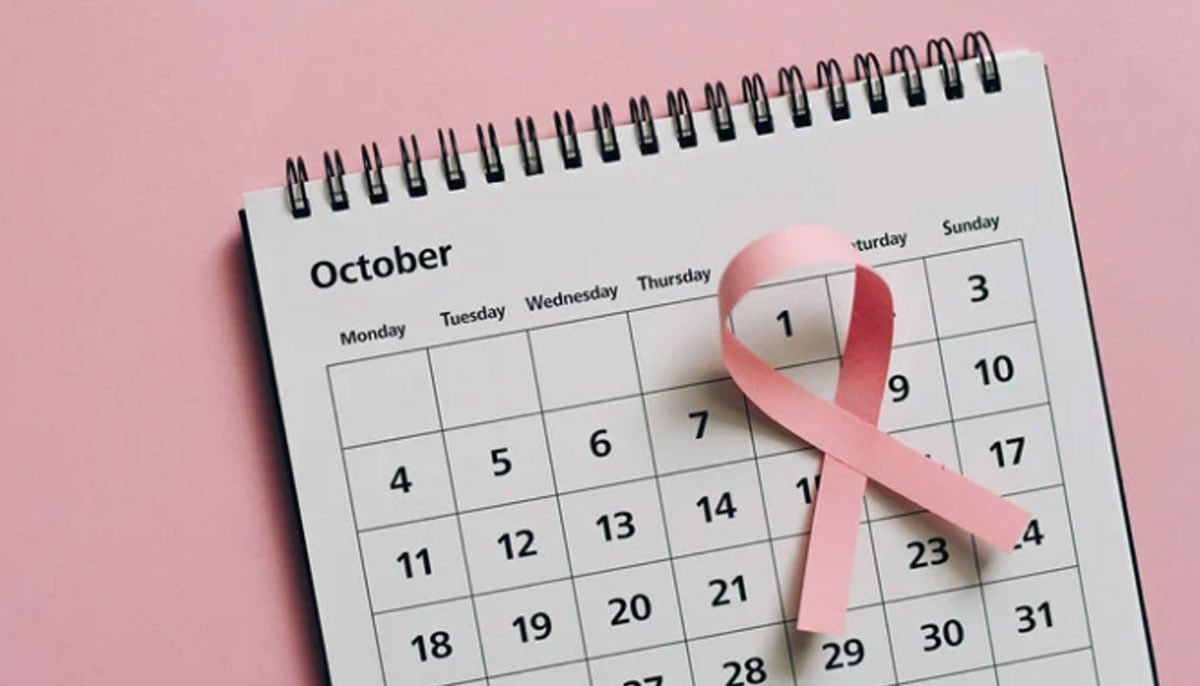 A representational image showing dates in the month of October on a calendar with a pink ribbon placed on it. — Canva