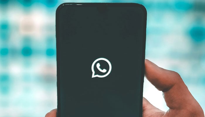 A representational picture showing a person holding a phone with the WhatsApp logo displayed on its screen. — Unsplash