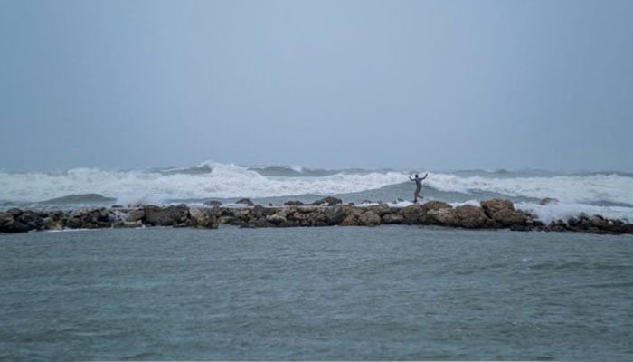 A representational image showing a man walking on the rocks amid strong waves. — Reuters/File