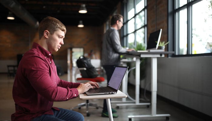 A representational image depicting two men working on computers while sitting and standing. — Unsplash/File