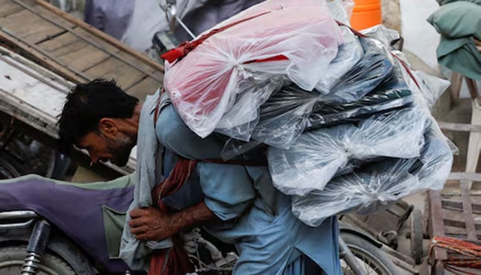 A labourer bends over as he carries packs of textile fabric on his back to deliver to a nearby shop in a market in Karachi on June 24, 2022. — Reuters