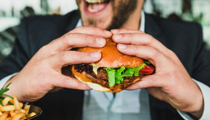 A representational image showing a man eating a burger. — Unsplash