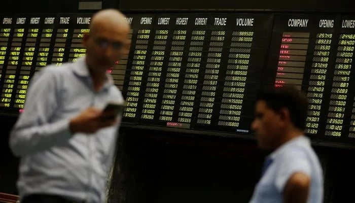 Brokers use their cell phones as they stand in front of electronic board displaying share market prices during a trading session in the halls of PSX in Karachi, on, June 12, 2017. — Reuters