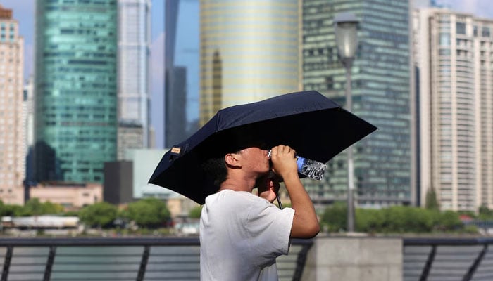 A man drinks from a water bottle under an umbrella as he walks on The Bund amid a red alert for heatwave, in Shanghai, China August 1, 2024.. — Reuters