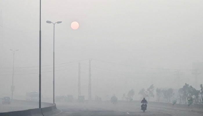 A man rides a motorbike along a street engulfed in dense smog, in Lahore on October 23, 2024. — AFP