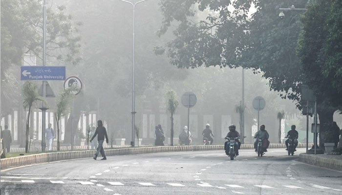 Commuters ride along a street engulfed in dense smog, in Lahore on October 23, 2024. — AFP