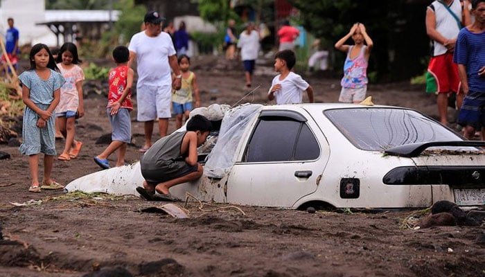 Residents look at a car buried by volcanic ash which cascaded into a village triggered by heavy rains brought about by Tropical Storm Trami at a village in Guinobatan town, Albay province South of Manila on October 23, 2024. — AFP