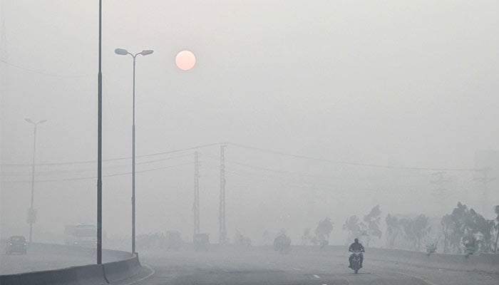 A man rides a motorbike along a street engulfed in dense smog, in Lahore on October 23, 2024.