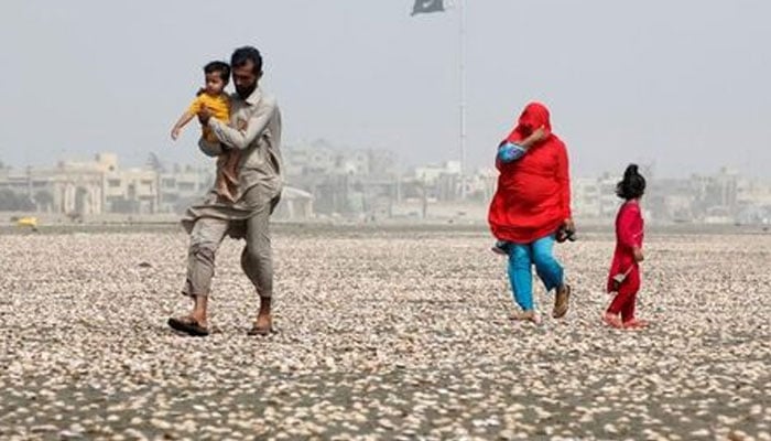 A woman covers her face with scarf to avoid heat while walking with her family along the beach on a hot  day in Karachi. — Reuters