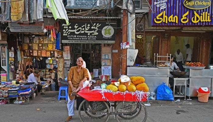 A fruit vendor standing along with his handcart in front of an Urdu literature bookshop at Urdu Bazar in the old quarters of Delhi on October 14, 2024. —AFP