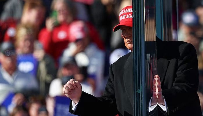 Republican presidential nominee and former US President Donald Trump gestures while touching the protective glass, during a campaign rally, in Lititz, Pennsylvania, US November 3, 2024. REUTERS