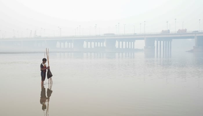 Faheem sets up a fishing trap, with the bridge over the River Ravi in the background, amid smog in Lahore, on November 5, 2024. —Reuters