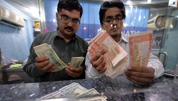 Money dealers count Pakistani rupees, right, and US dollars at a currency exchange in Islamabad on March 12, 2014. — AFP