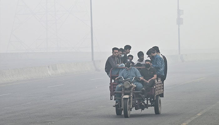 Commuters ride along a road engulfed in smog in Lahore on November 8, 2024. — AFP