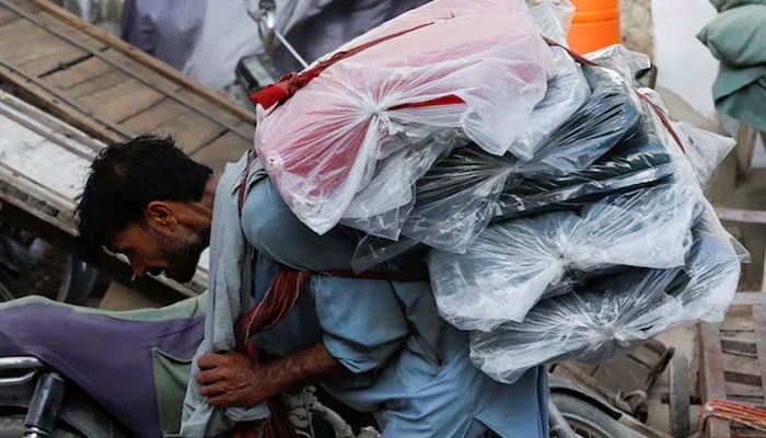 A labourer bends over as he carries packs of textile fabric on his back to deliver to a nearby shop in a market in Karachi on June 24, 2022. — Reuters