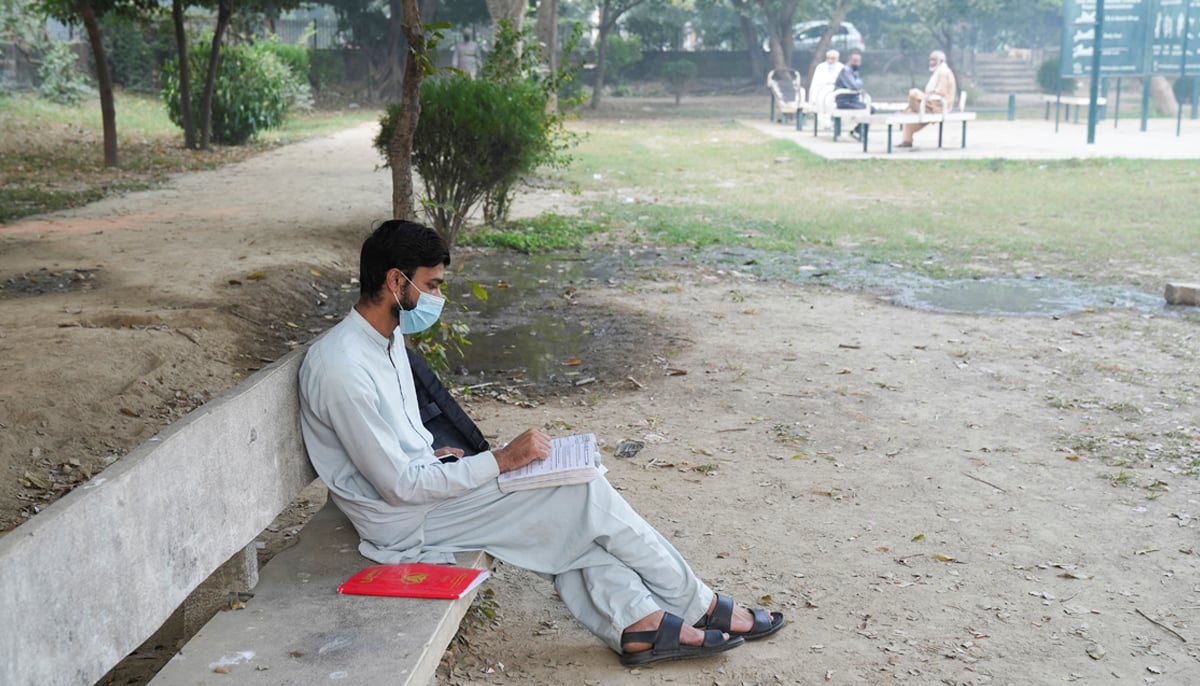 A man, uses a face mask to avoid smog, while reading book at a park in Lahore on November 5, 2024. — Reuters