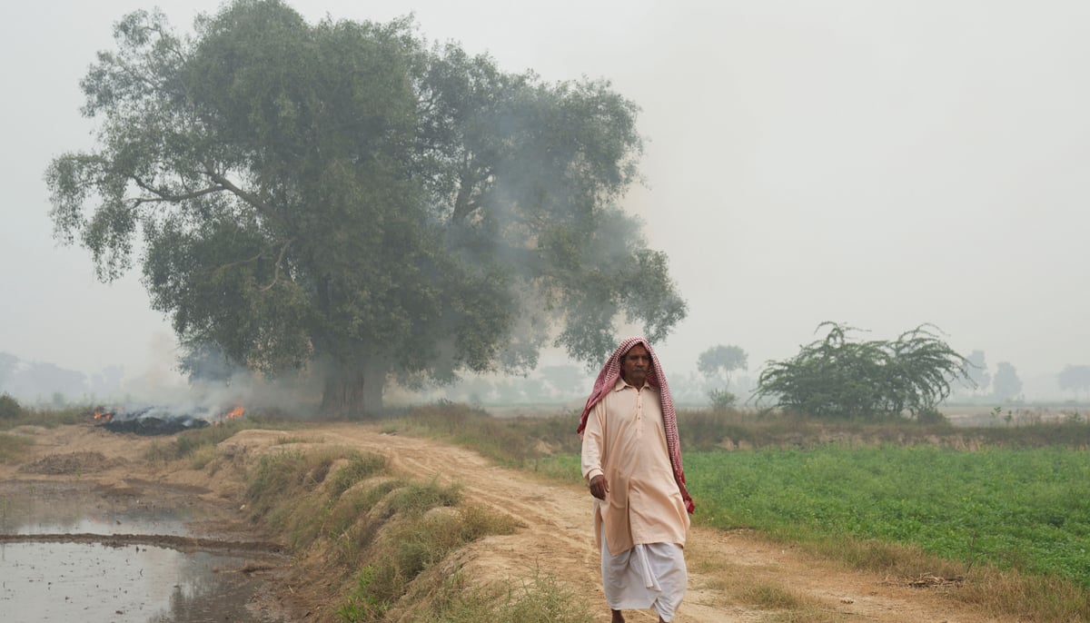 Ghulam Muhammad walks near smoke from burning debris in the background, on the outskirts of Lahore on November 7, 2024. — Reuters