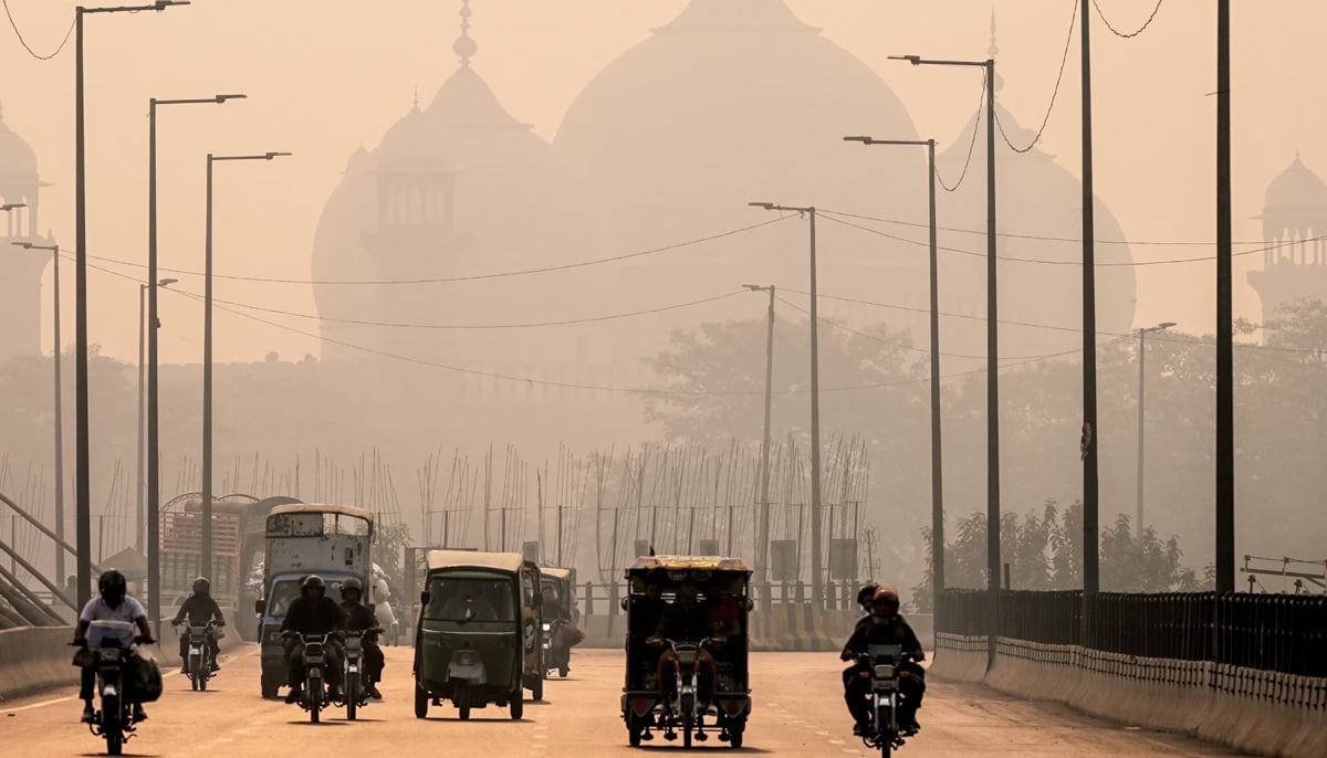 Commuters ride along a street engulfed in smog, in Lahore on November 5, 2024. — AFP