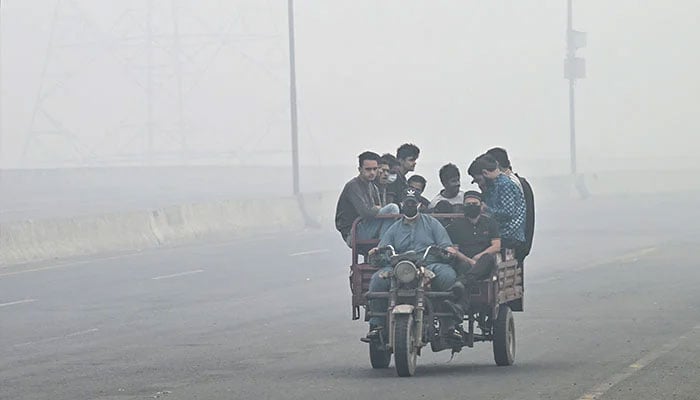 Commuters ride along a road engulfed in smog in Lahore on November 8, 2024. — AFP