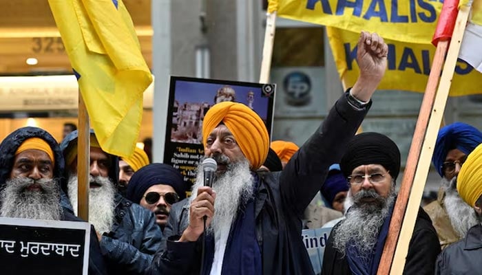 A demonstrator uses a microphone as others hold flags and signs as they protest outside Indias consulate. — Reuters