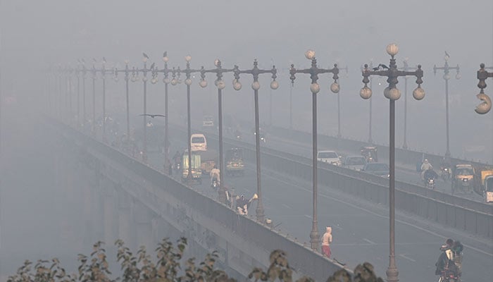 Commuters ride along a street engulfed in smog in Lahore on November 18, 2024. — AFP