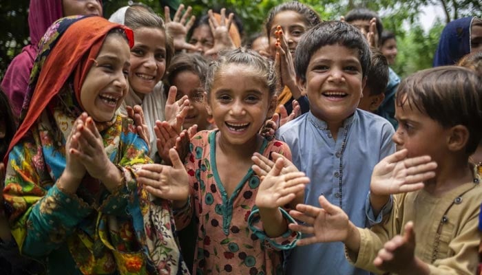 An undated image shows a group of children laughing while clapping their hands. — UNICEF/File